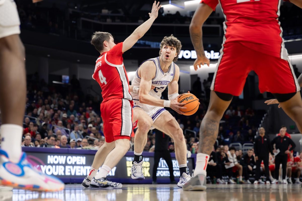 A Northwestern player drives aggressively into the lane, gripping the ball tightly as an Ohio State defender closes in with both hands up to block. 