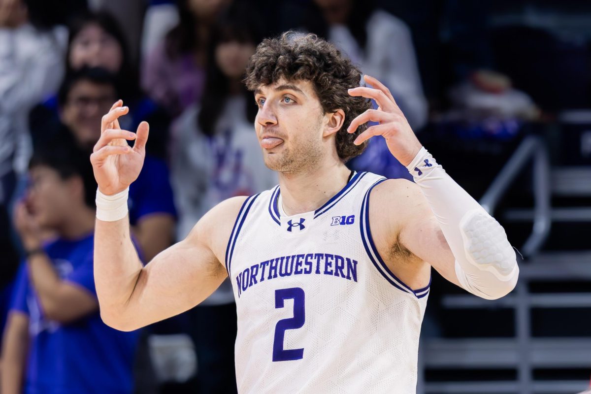 A Northwestern player gestures toward teammates after a whistle, tongue slightly out, with the home crowd blurred in the background. 