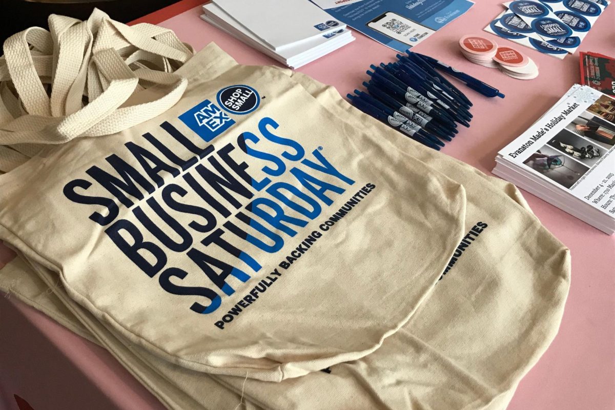 A tote bag reading “Small Business Saturday” is set upon a table among pens and stickers.