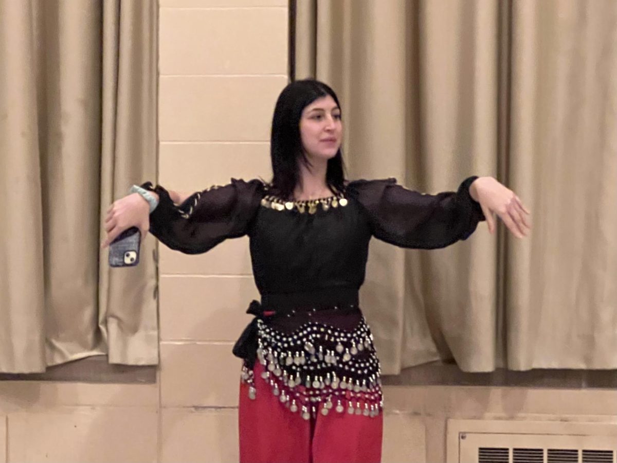 A person wearing a black top, red pants and a coin belt raises her arms.