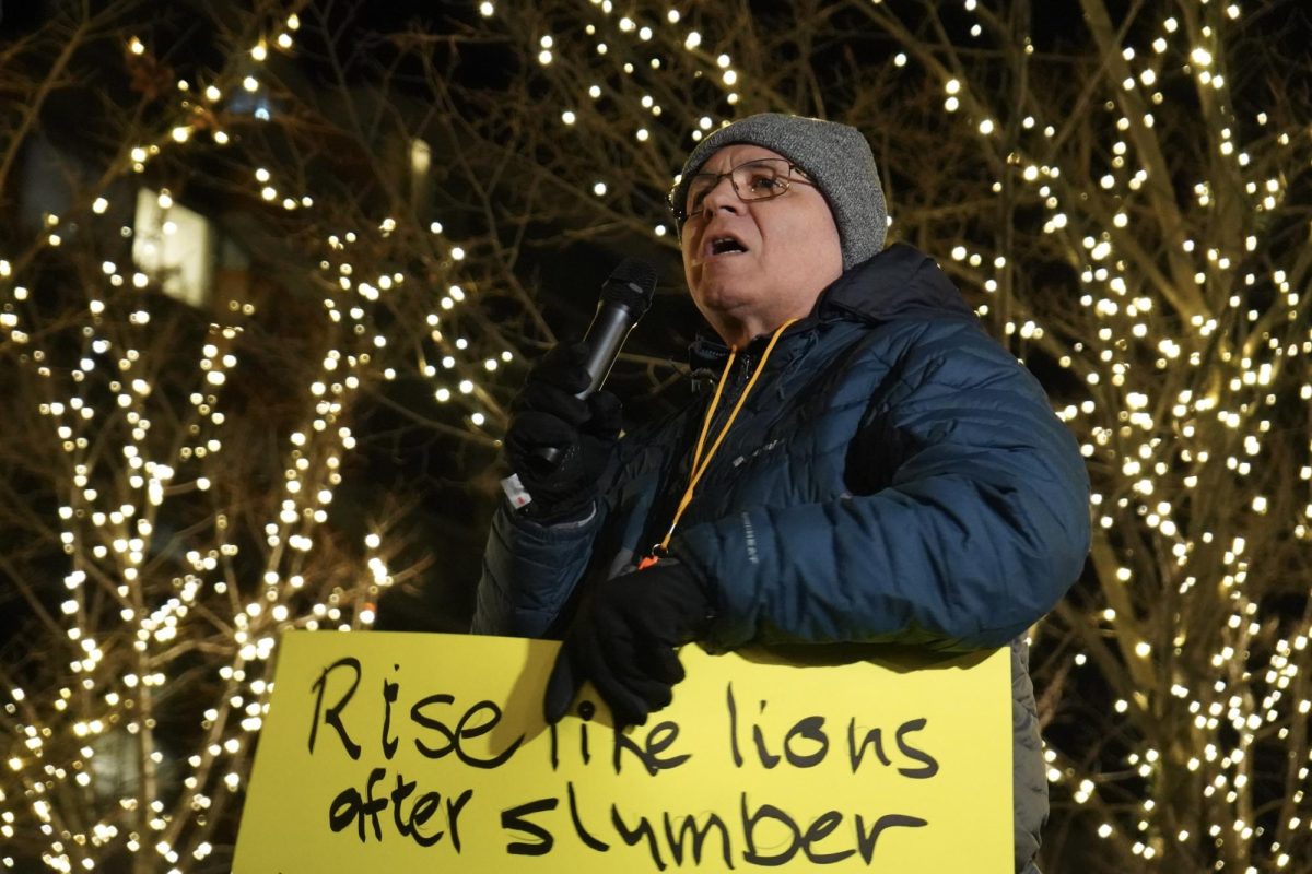 A person holds a yellow sign while speaking into a microphone.