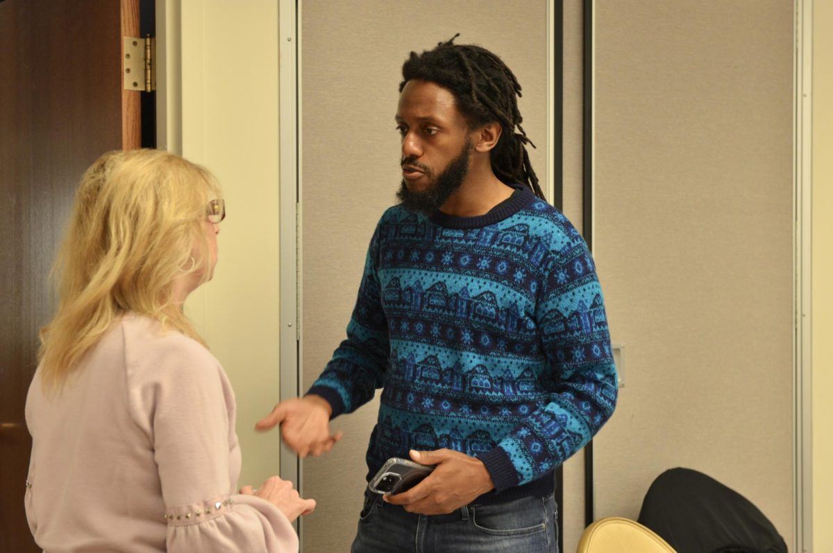 A person in a blue sweater converses with someone in a pink shirt.