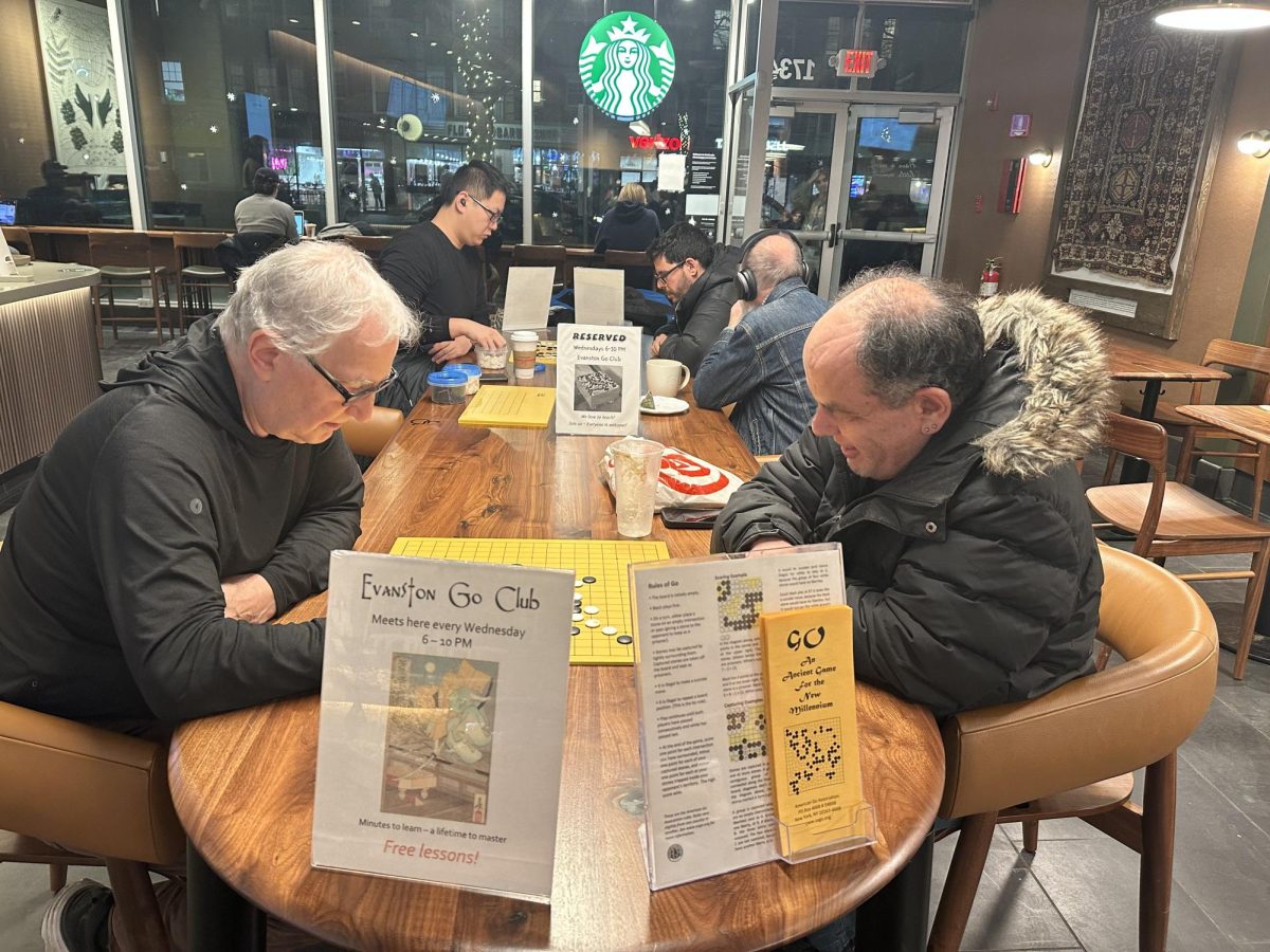 Two men sit at a table playing the board game Go.