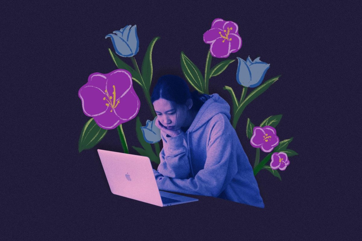 A person looks at a computer against a dark background surrounded by purple and blue flowers.