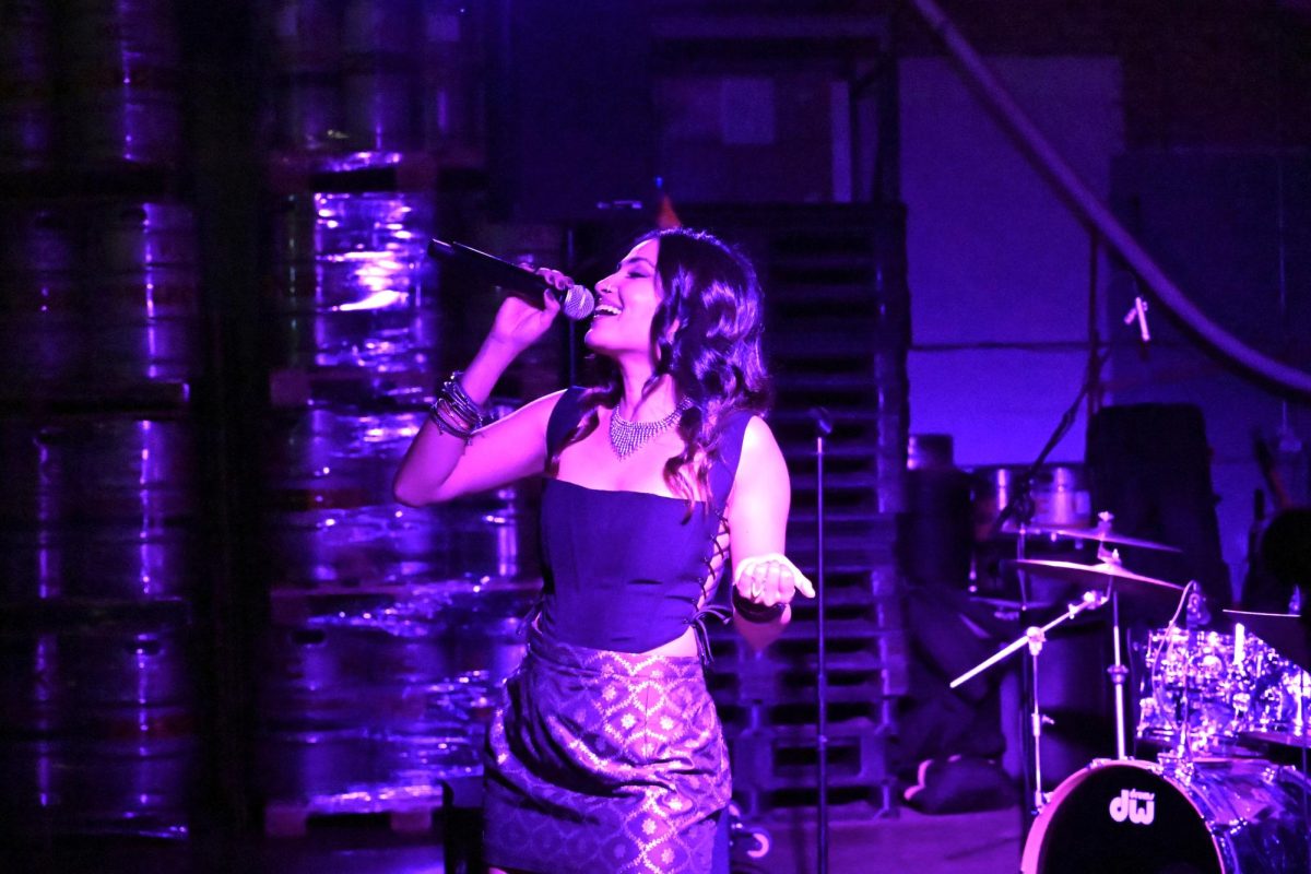 A singer holds the mic close to their mouth and lifts their other hand in the air.