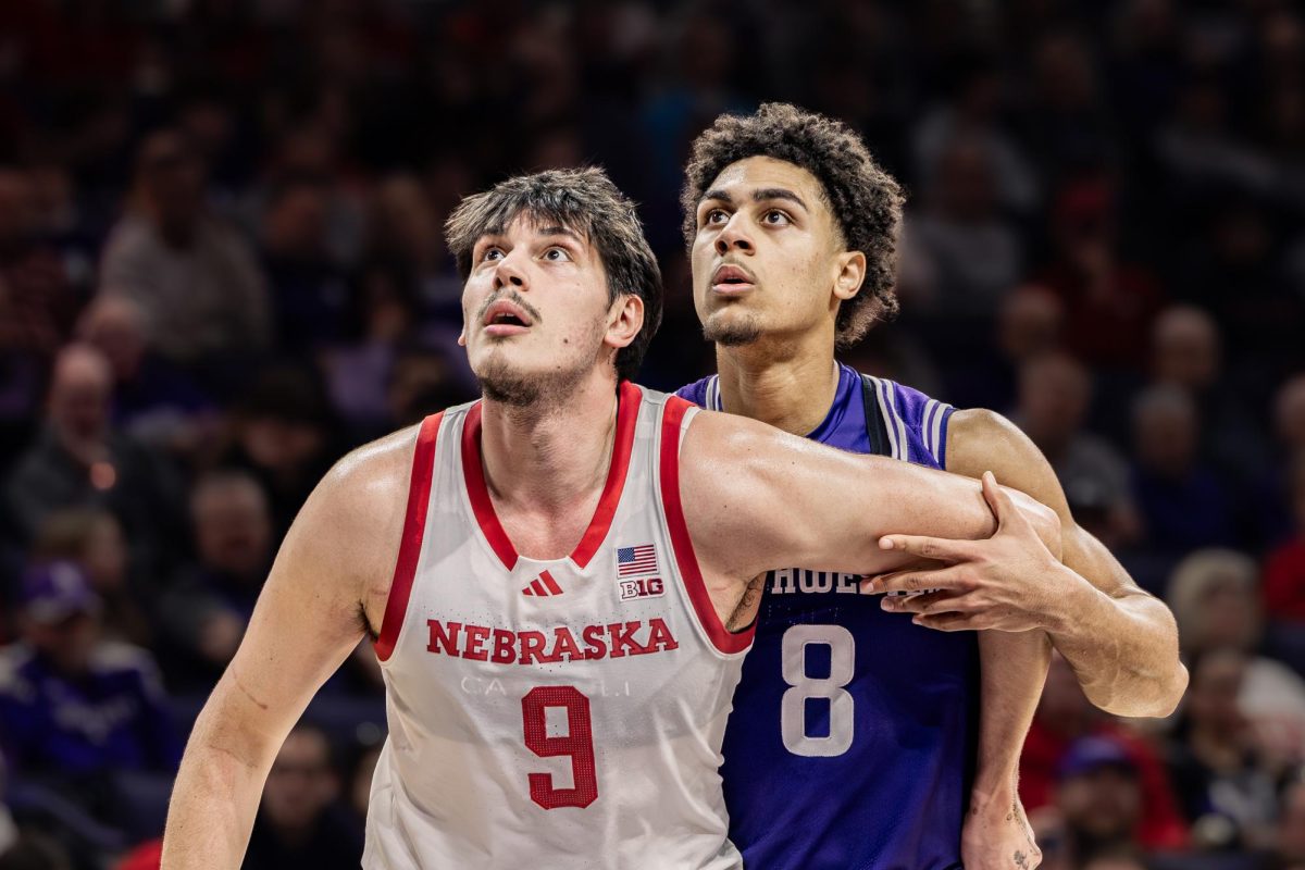A Northwestern defender positions behind a Nebraska player under the rim, both looking upward as they track a rebound.