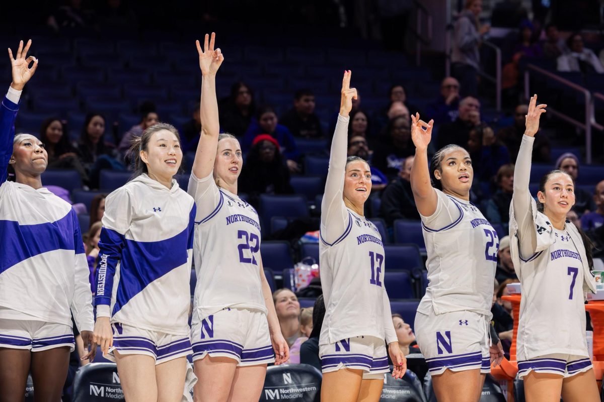 Northwestern players on the bench stand and raise three fingers in celebration after a successful three-point basket.