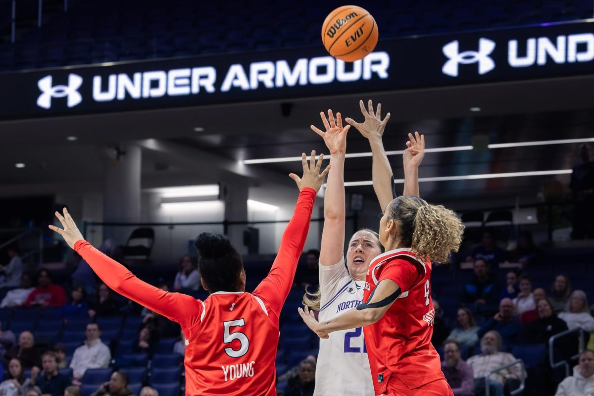 A Northwestern player rises for a contested jump shot as two Rutgers defenders reach to block the attempt.
