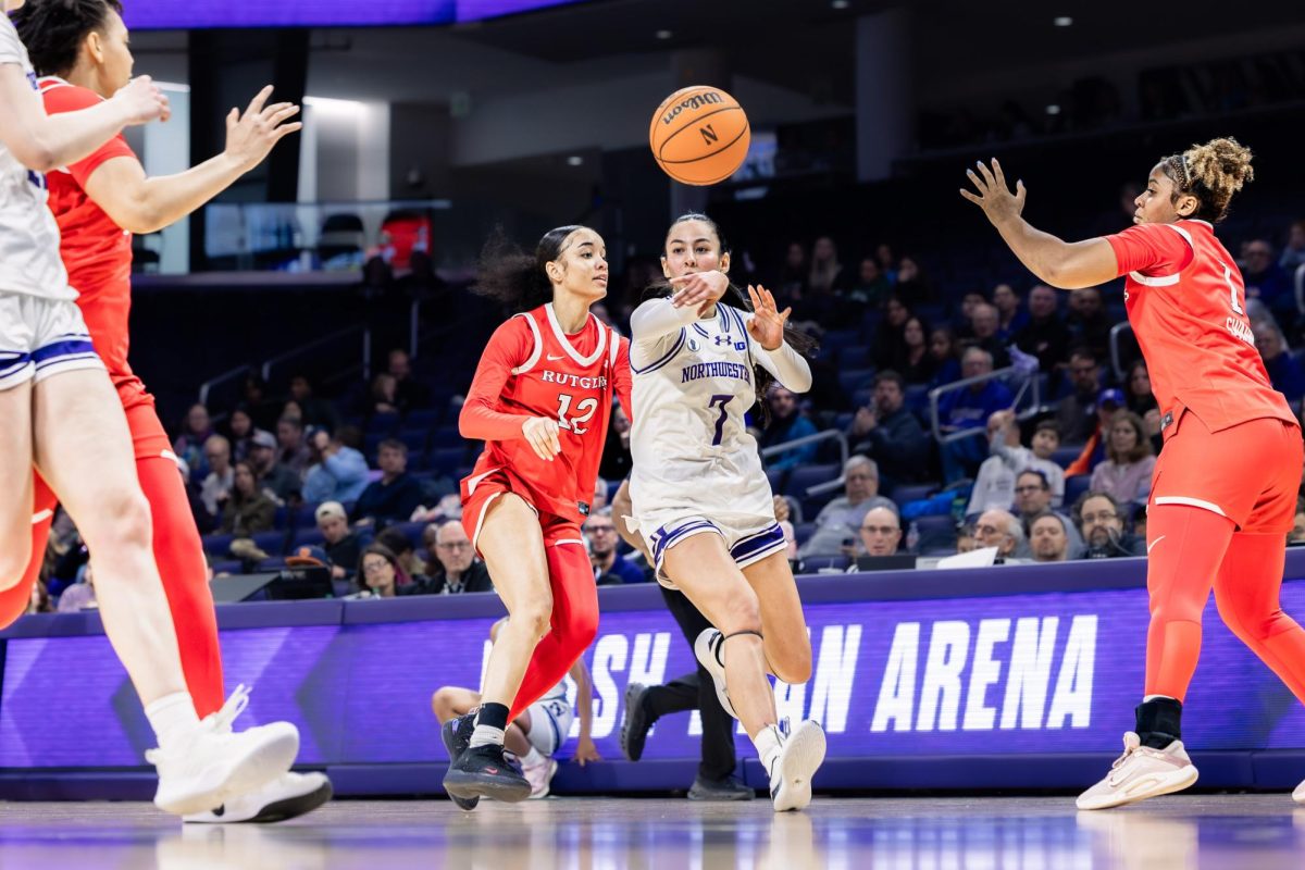 A Northwestern guard passes the ball forward in transition as a Rutgers defender tracks the play.