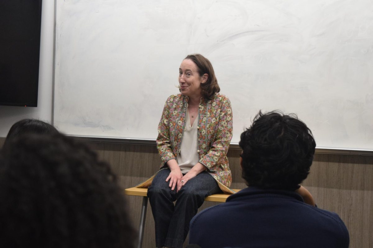 A person sits on a desk and smiles, framed by two audience members.