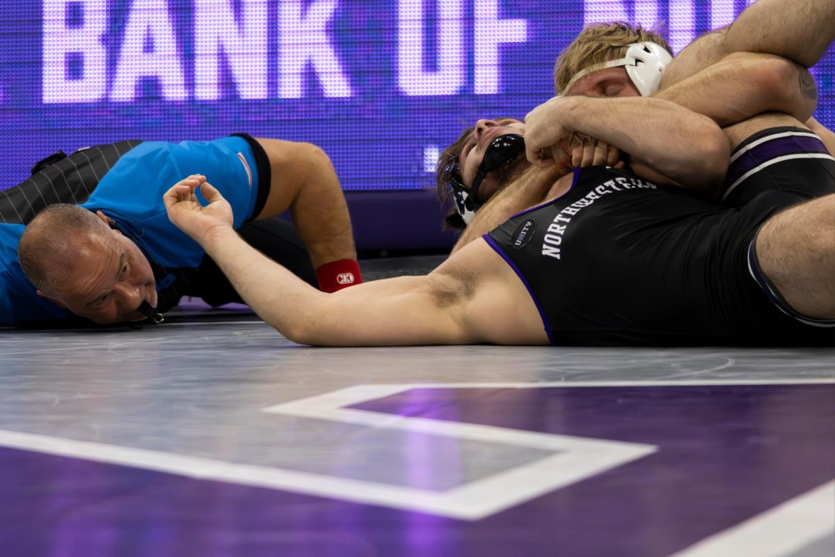 A wrestler in a black singlet’s shoulders are held back onto the mat.
