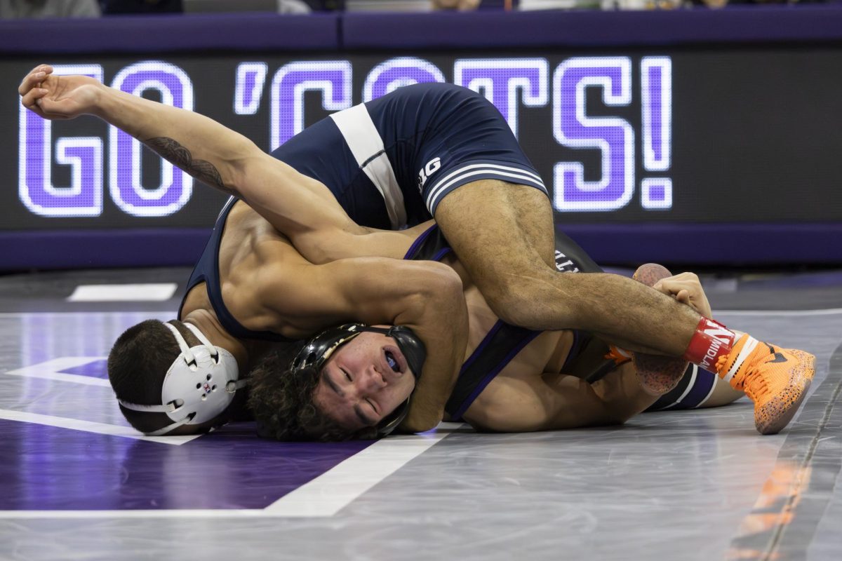 A wrestler in a blue singlet turns a wrestler in a black singlet onto his back.