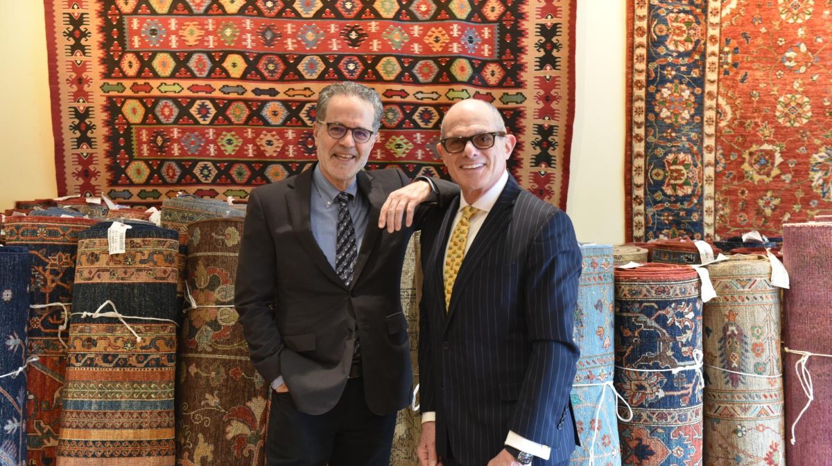 Two men pose in front of their rugs.