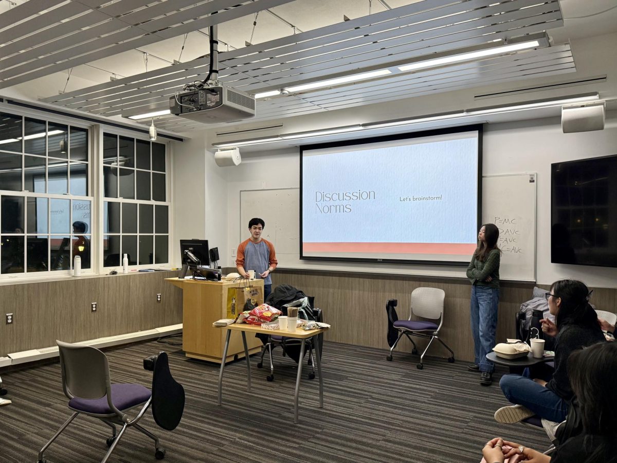 Two people present next to a projected slideshow in front of a room of people.