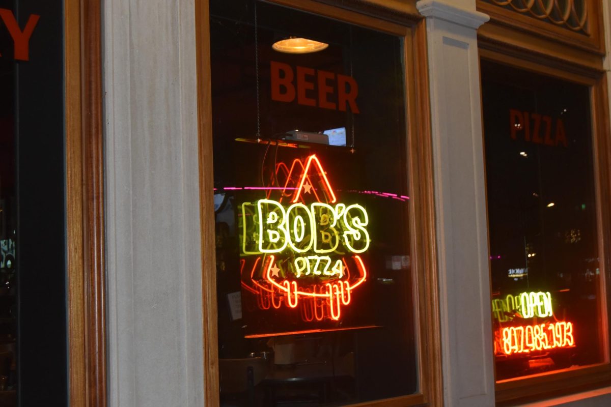 A neon sign reading Bob’s Pizza hanging in a window.