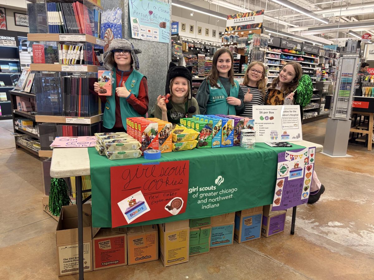 Girl Scouts stand behind a table selling cookies inside an arts and crafts store.