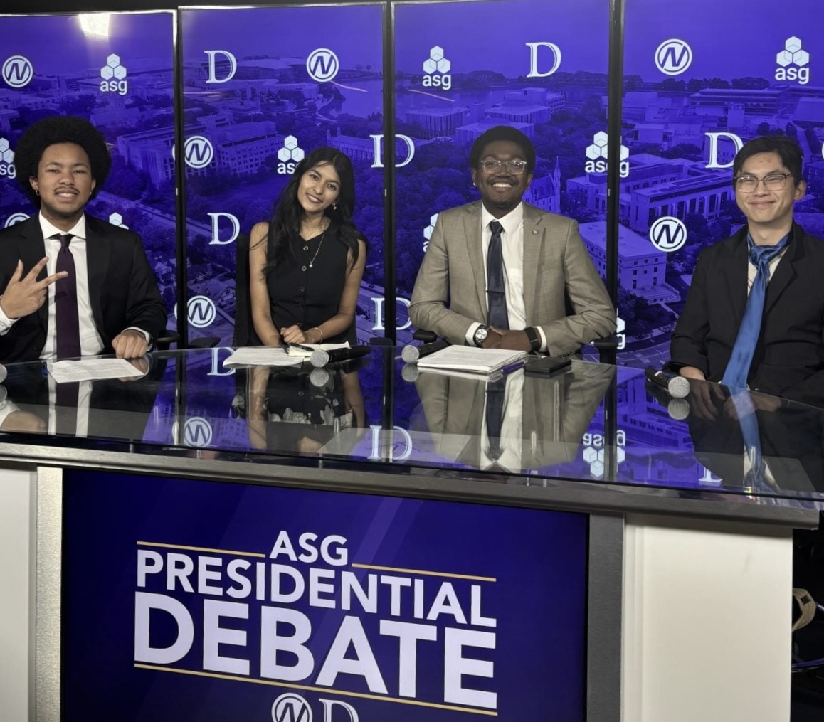 Four people pose for a picture while sitting at a roundtable.
