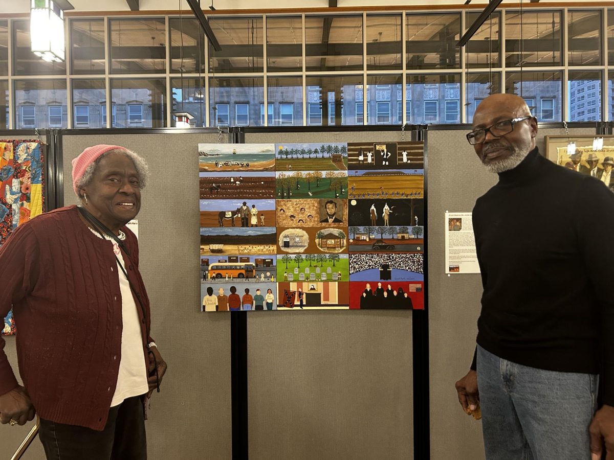 Two people stand in front of an art piece.