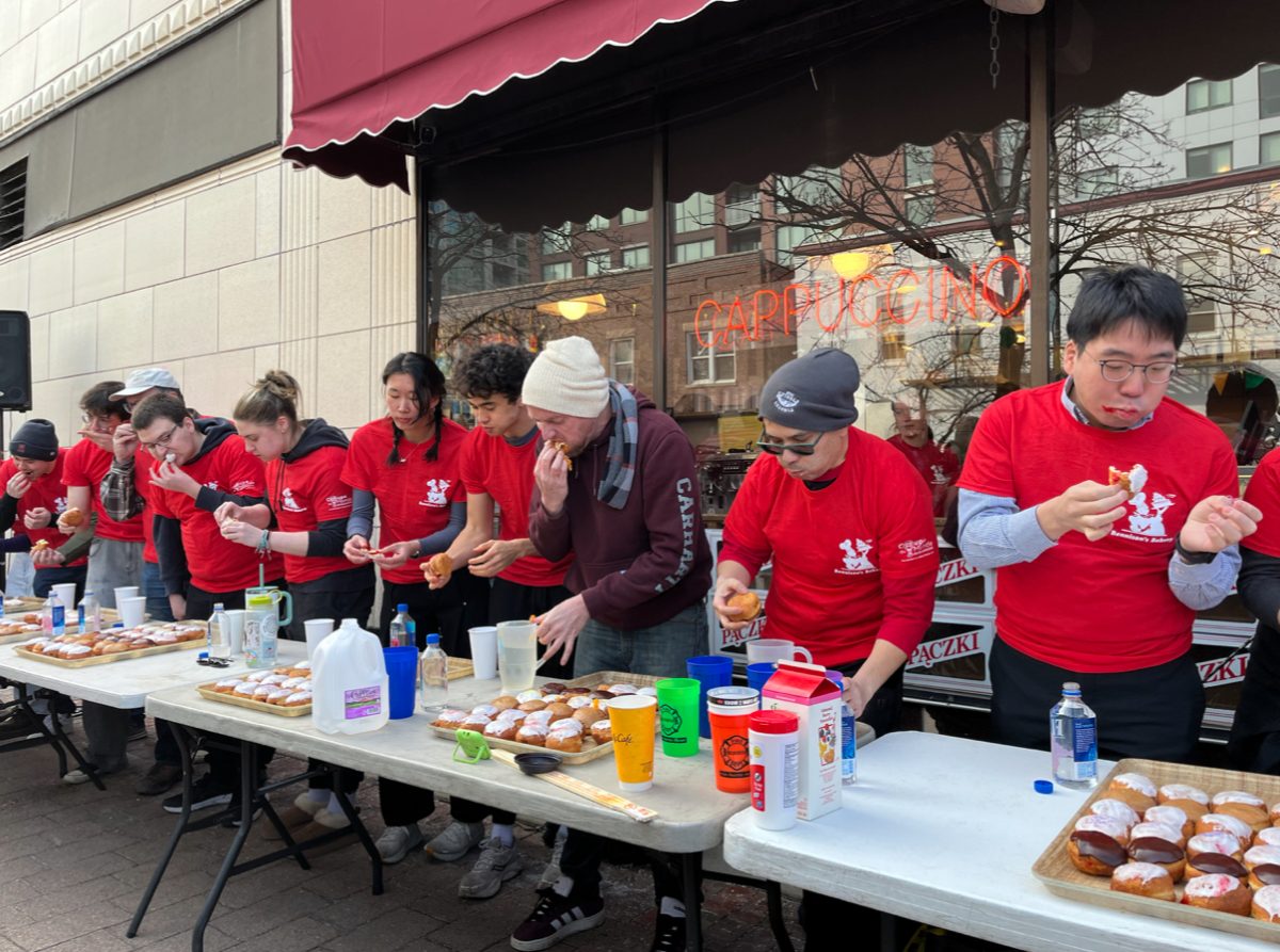 A group of people lined up behind folding tables, eating donuts.