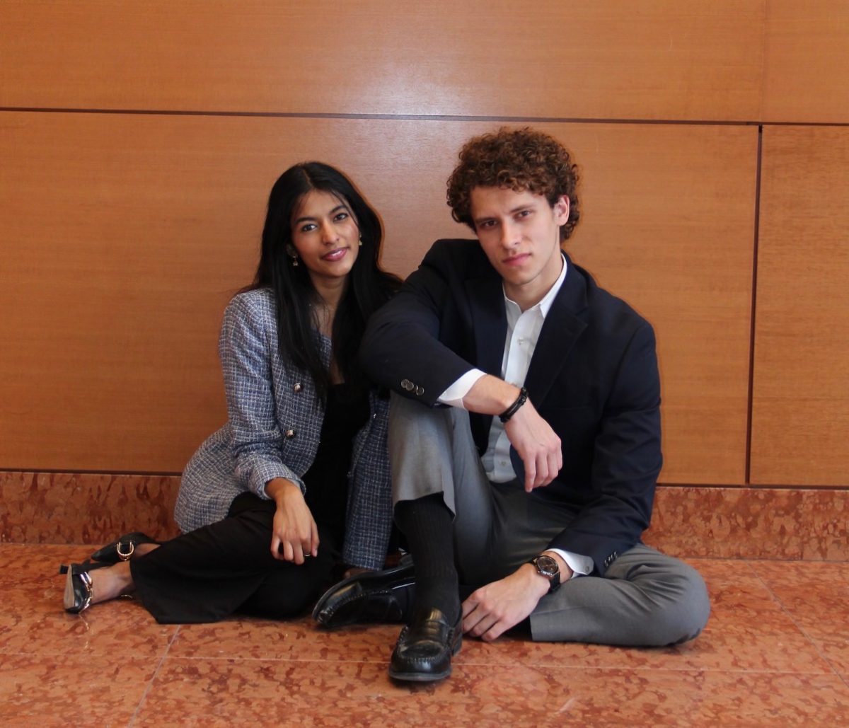 Two people sitting by a wall.