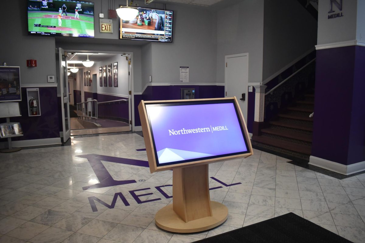 The photo shows the inner lobby of Northwestern University’s Medill School of Journalism, with a kiosk displaying “Northwestern | Medill.”