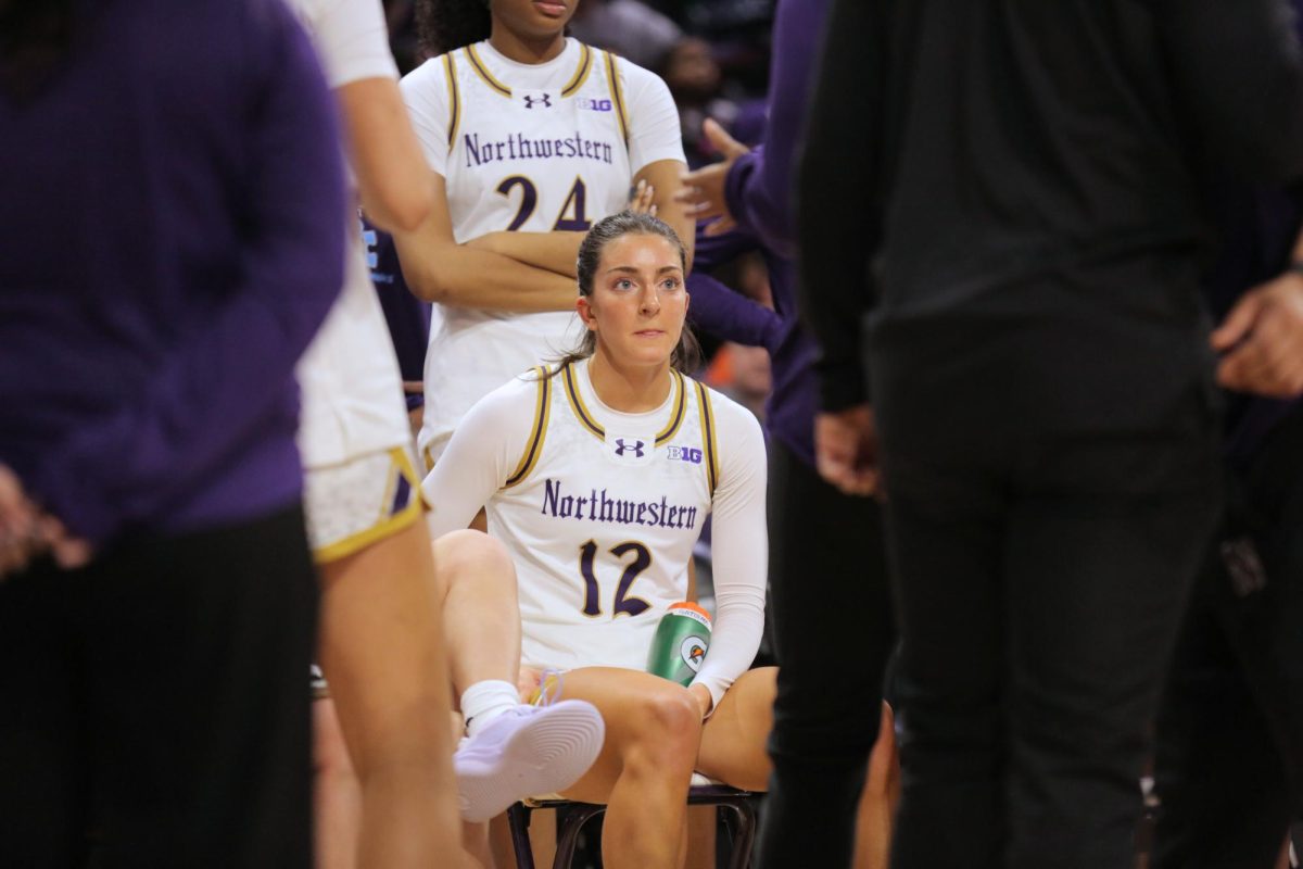 A person in a white jersey sits in a crowd, framed by others on either side.