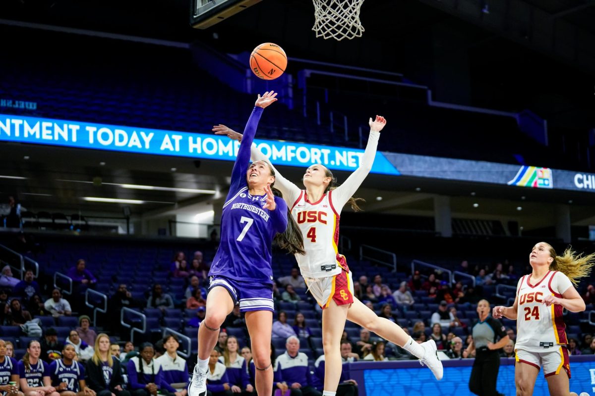 A basketball player stretches up to shoot while an opposing player attempts to make a block.