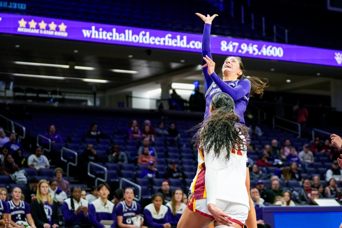 A basketball player stretches up for a shot attempt while an opposing player tries to block them.