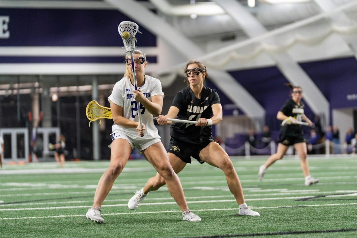 A lacrosse player runs with the ball, while an opposing player stands behind them.