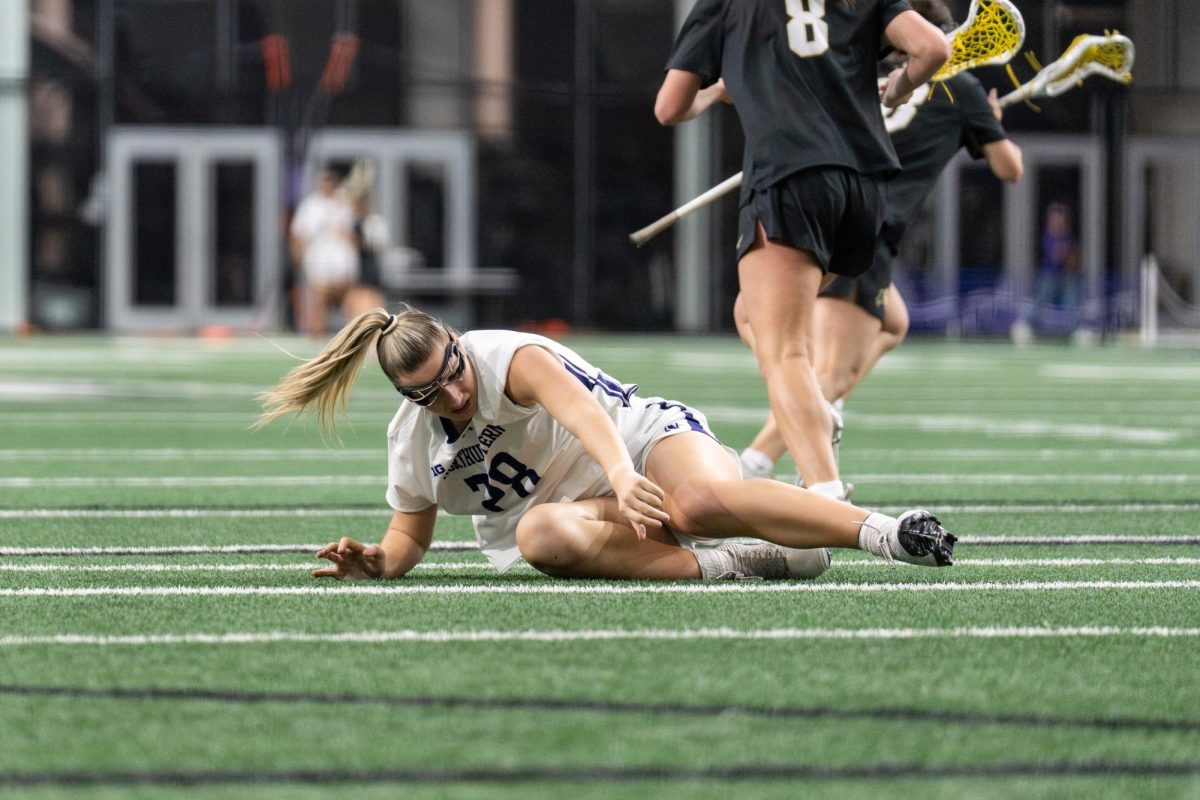 A lacrosse player starts to lift themself up after falling.