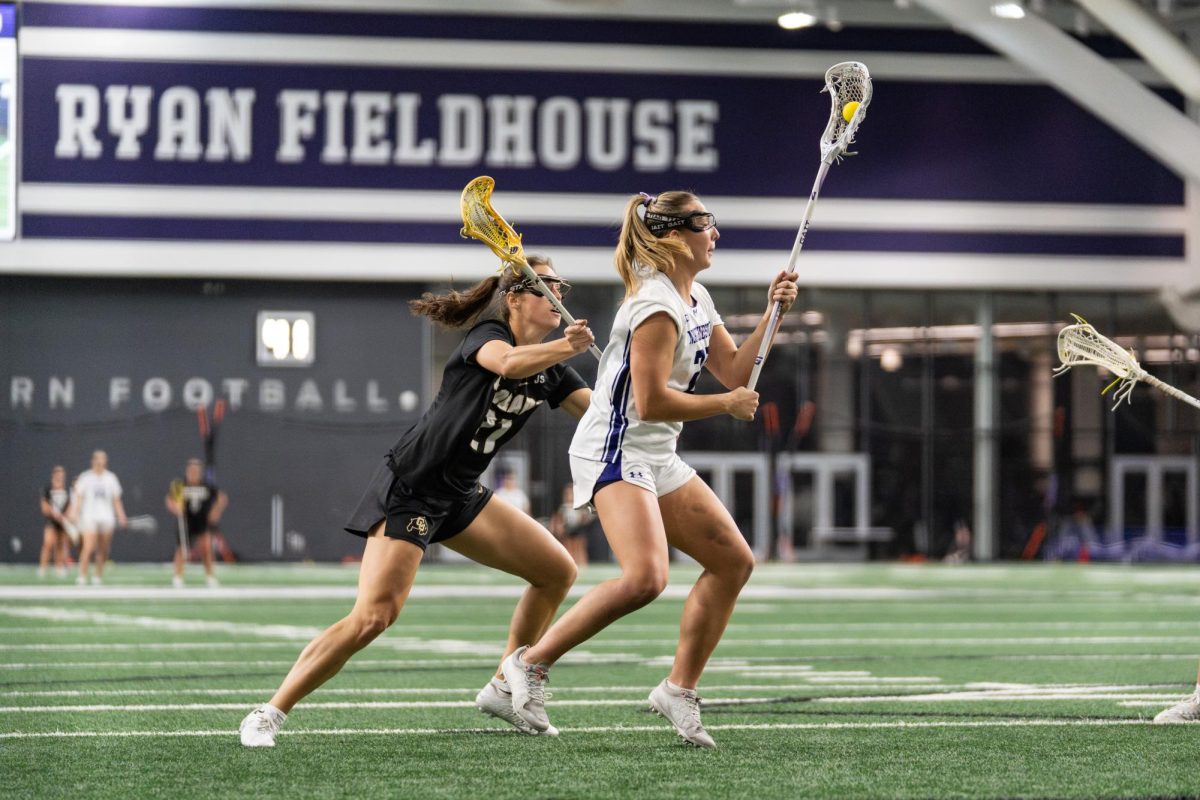 A lacrosse player takes the ball down the field as an opposing player chases them.