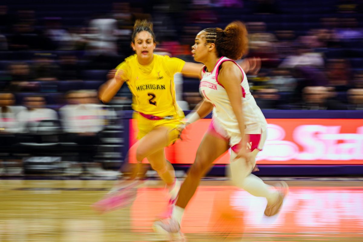 A player wearing white dribbles a basketball in front of a blurred crowd.