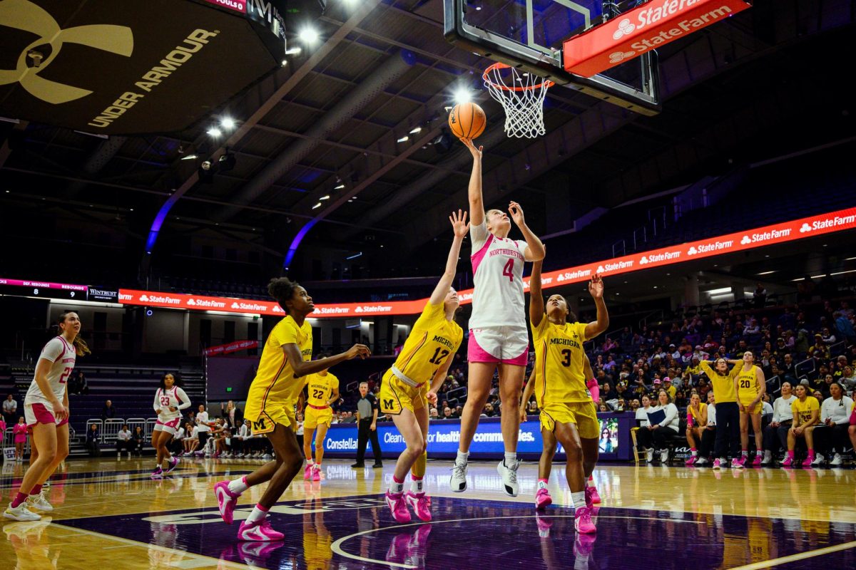 A player in white jumps up towards a basketball hoop, surrounded by players in yellow.