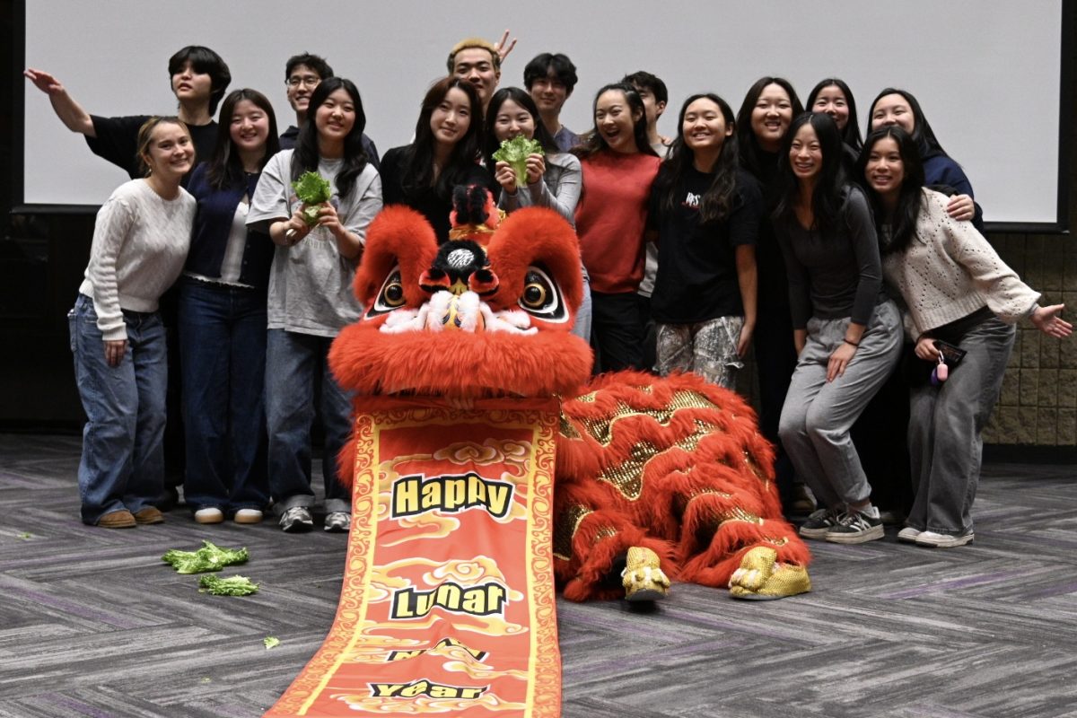 Participants pose for a picture with a red lion costume. A banner reads “Happy Lunar New Year.”