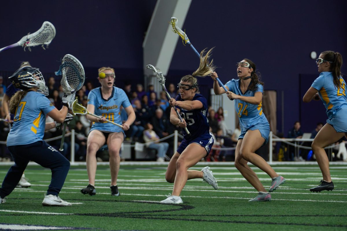 A player in a purple jersey shoots a ball past a goalkeeper in a blue jersey.