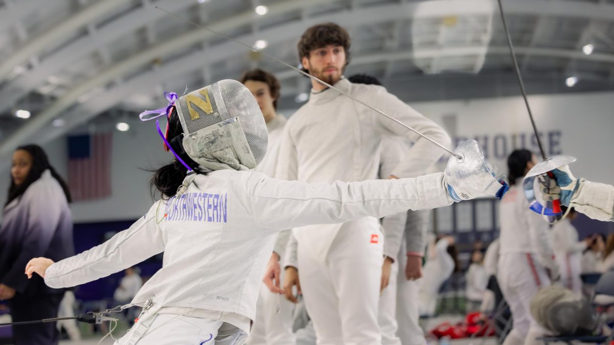 A Northwestern fencer lunges out fully while another fencer looks on.