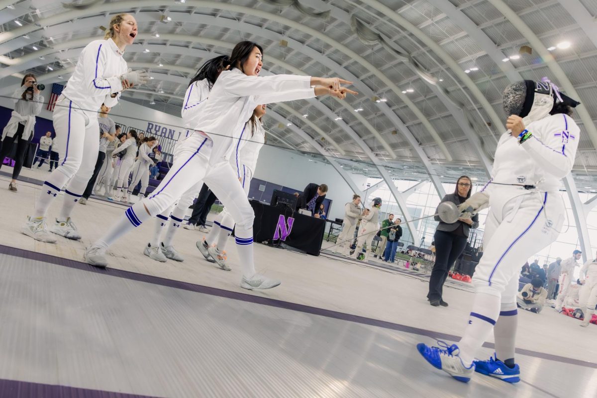 Northwestern fencers celebrate after a bout, yelling and pointing at each other.