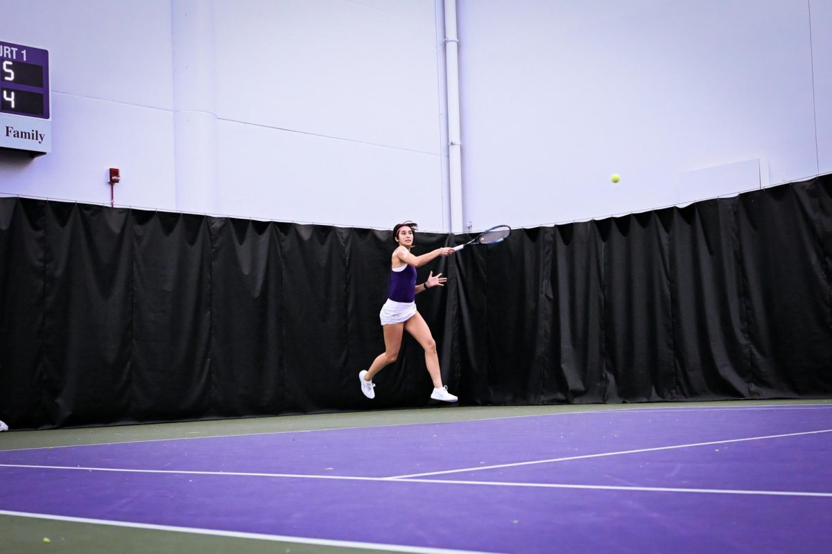 A tennis player jumps in the air while hitting a forehand.