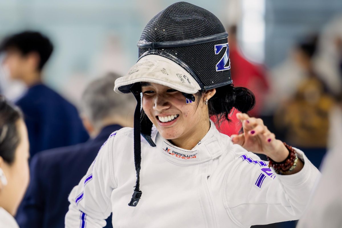 A fencer smiles with a mask resting on top of their head.