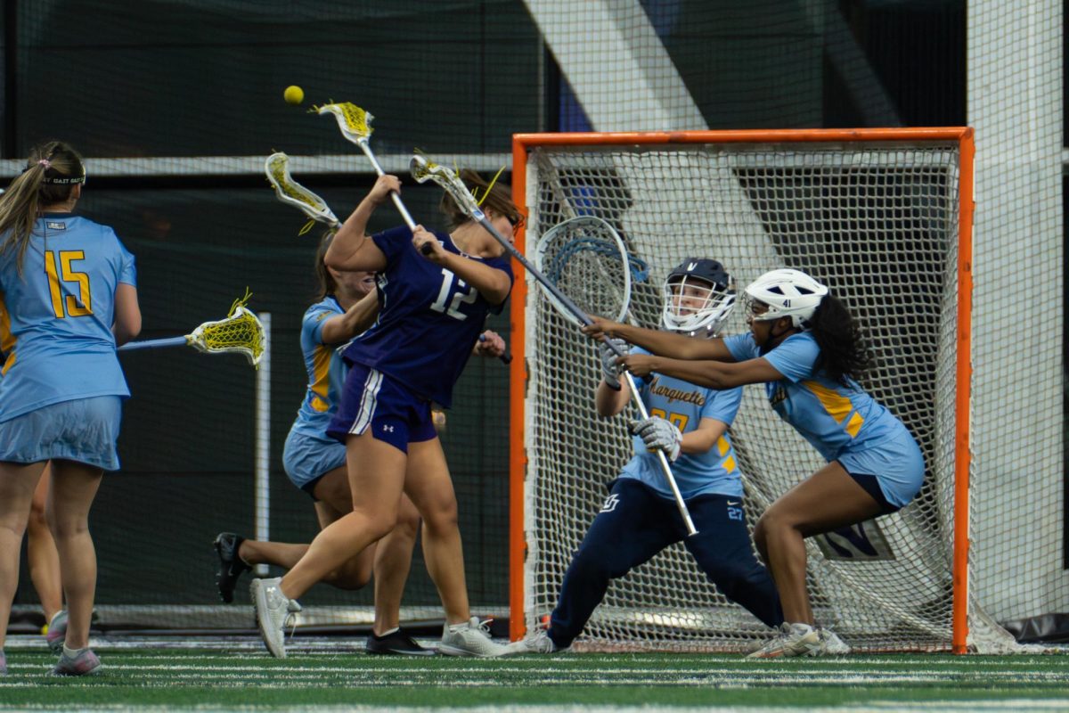 A player in a purple jersey shoots behind their back with three defenders in front of them.