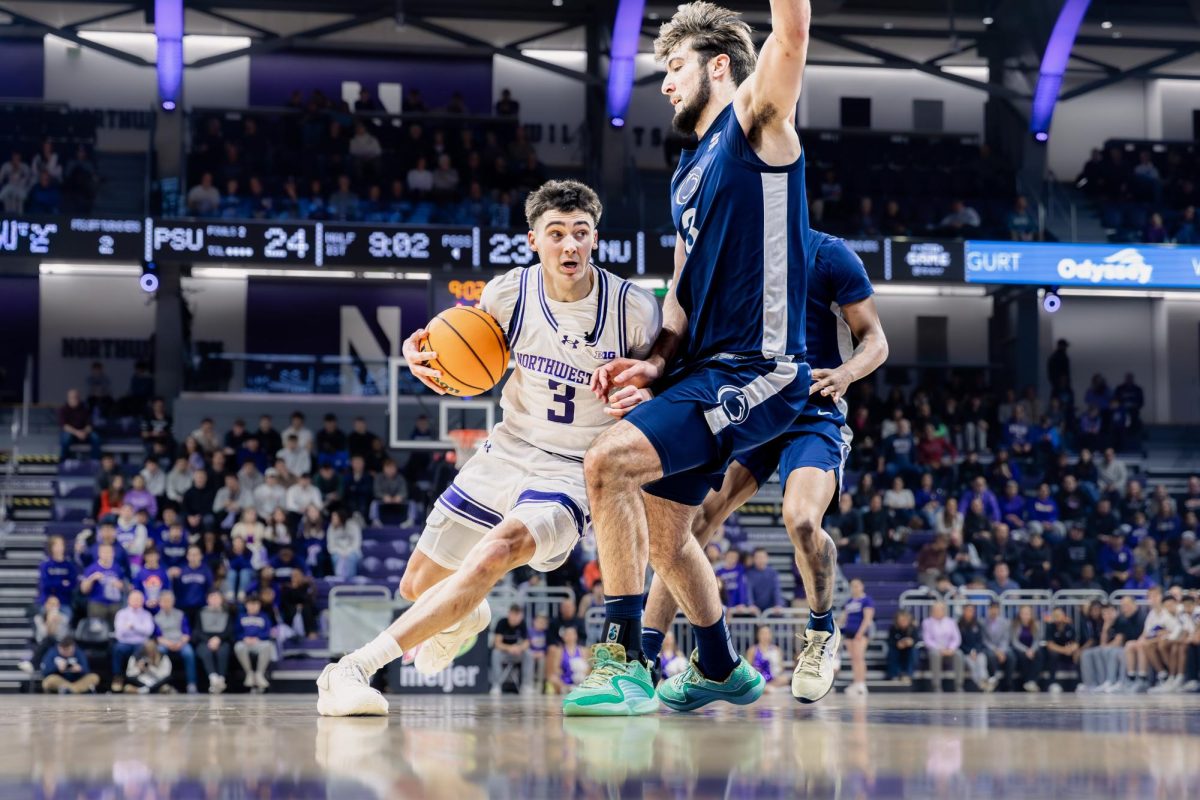 A Northwestern basketball player holding the ball and wearing white pushes past a defender in blue.