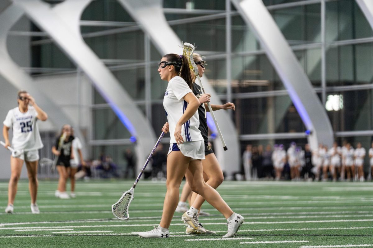 Two lacrosse players from opposing teams walk past each other, appearing to be back-to-back.