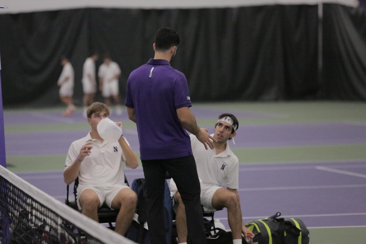 A person in a purple shirt talks to two people in white shirts who are sitting.