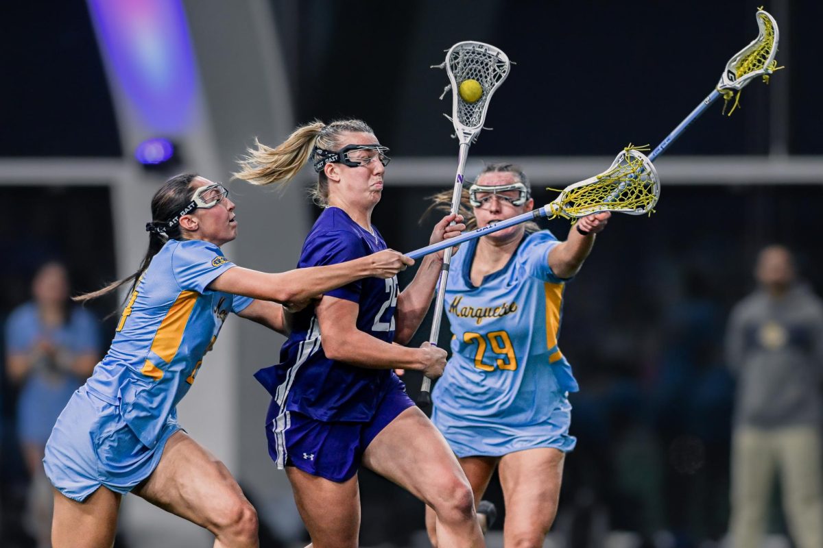 A Northwestern attacker pushes between two defenders with their sticks extended.