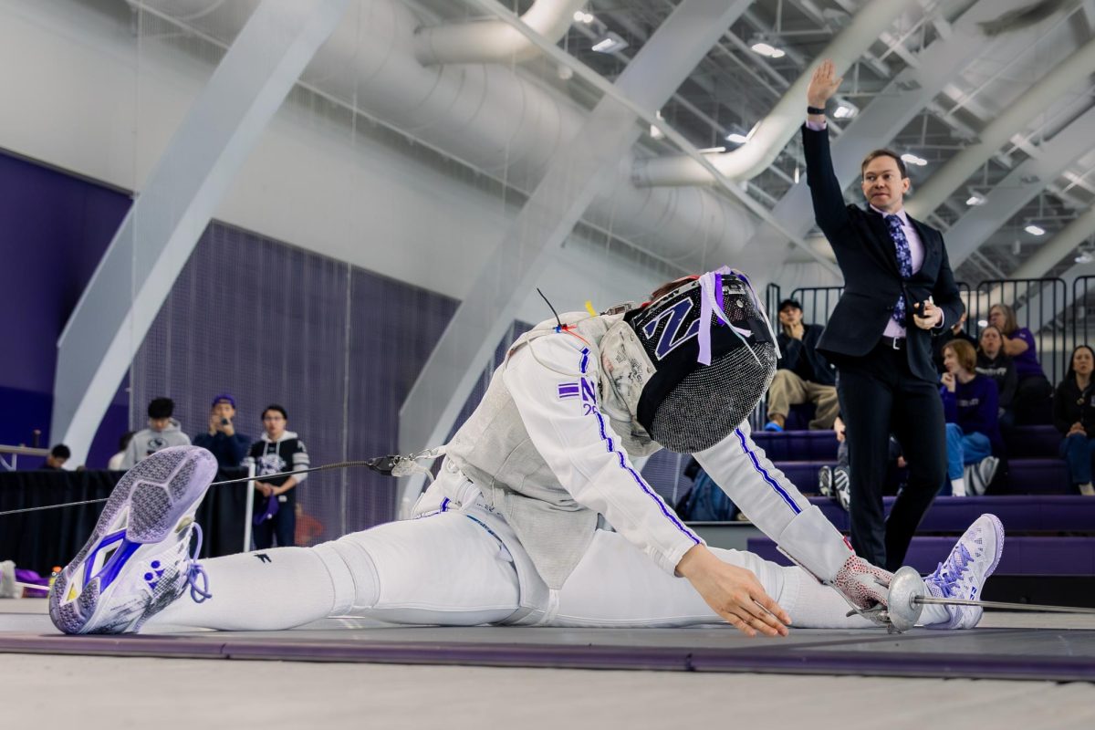 A Northwestern fencer sits in a split with their arms out between their legs.