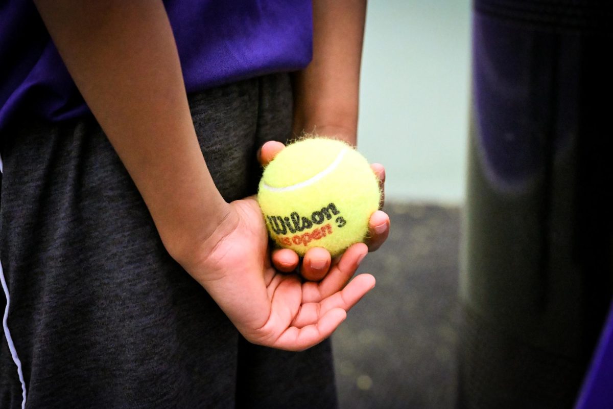 A child holds a tennis ball behind their back.