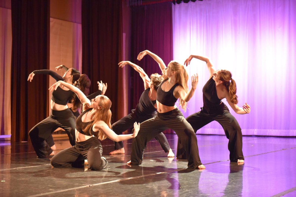 Six dancers dressed in black curve their bodies and arms.
