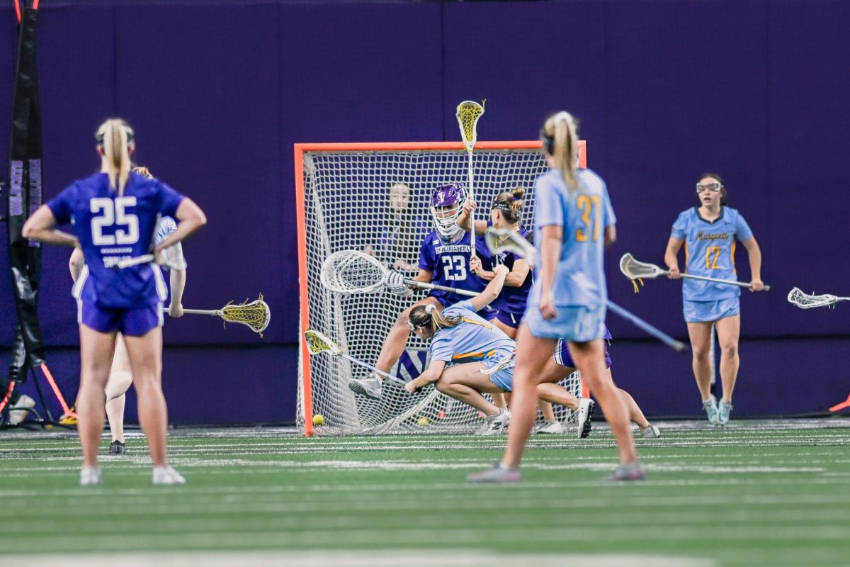 An attacker in blue shoots falls while being closely defended by a defender in purple.
