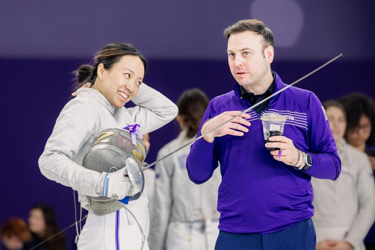 A Northwestern fencer smiles while a coach in purple talks to them.