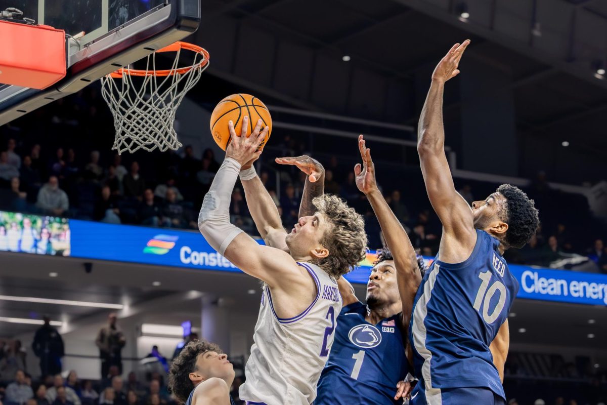 A Northwestern basketball player extends the ball to the rim while being contested by two defenders.